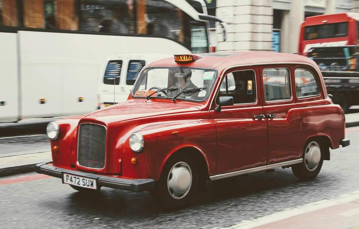 Taxi londonien rouge circulant en rue urbaine avec plaque de taxi éclairée