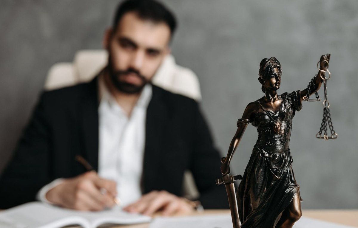 Homme en costume noir écrivant à un bureau avec une statue de justice en bronze