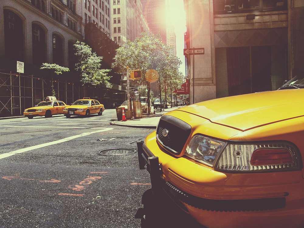 Des taxis jaunes circulent sur une avenue urbaine ensoleillée