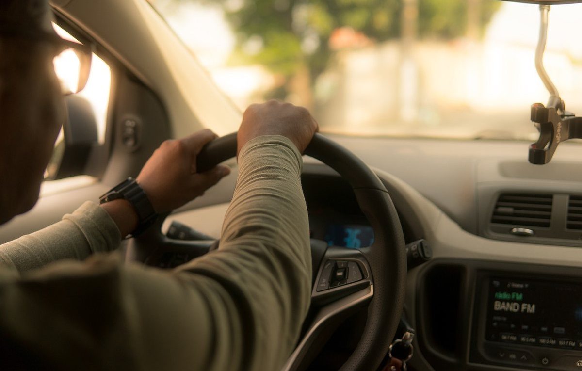 Un conducteur tient le volant, le tableau de bord et la radio sont visibles
