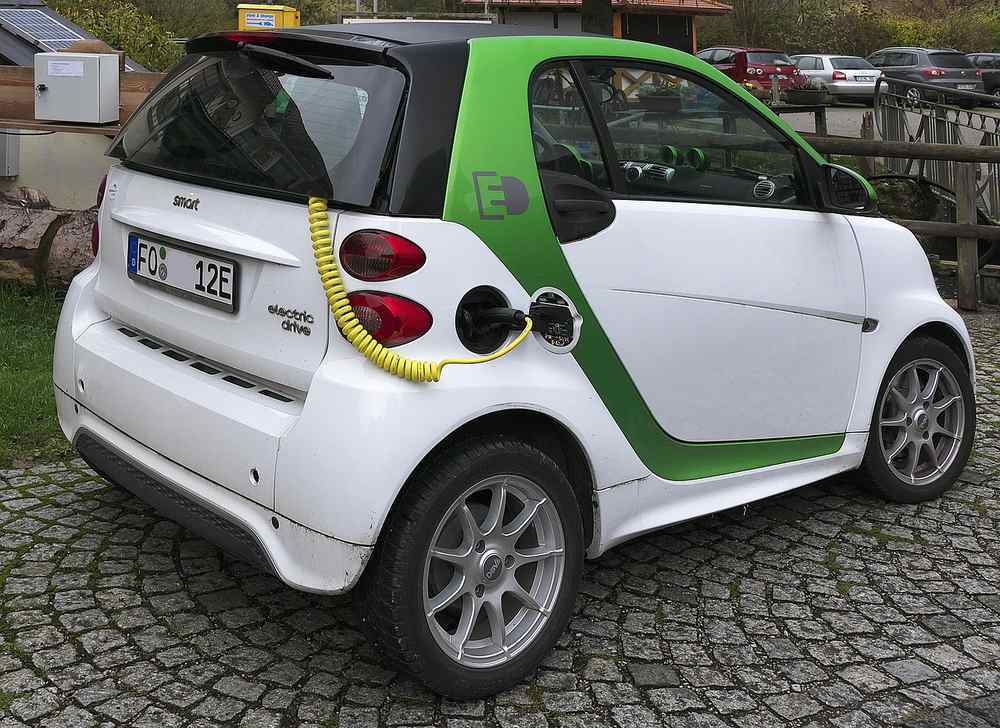 Une petite Smart blanche et verte branchée sur du gravier