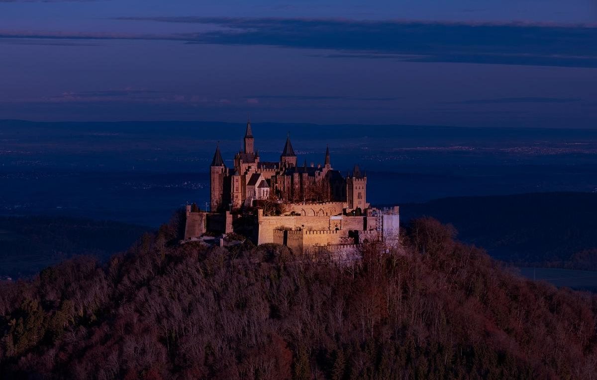 Un château fortifié dominant une colline boisée au crépuscule