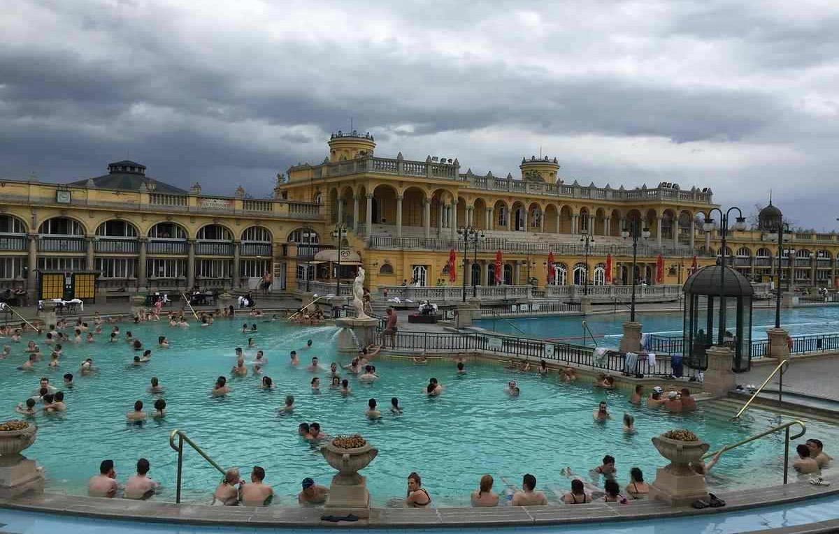 Baigneurs profitent d'un grand bassin thermal sous un ciel nuageux