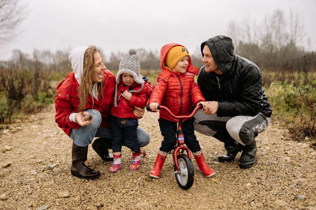 Famille souriante avec enfants en rouge sur un vélo miniature dans un paysage gris